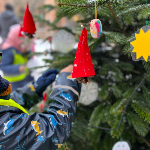 Foto zeigt Kinderhände, die den Weihnachtsbaum schmücken