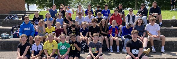 Ca. 50 Schülerinnen und Schüler sitzen bei Sonnenschein auf der Tribüne des Aleestadions in Schleswig.