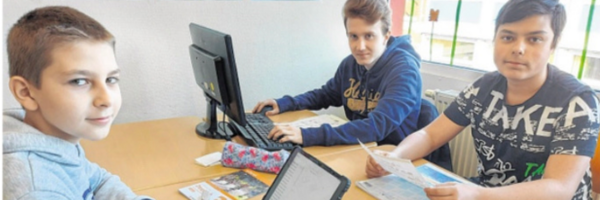 Foto aus den Schleswiger Nachrichten. Drei Schüler sitzen im Unterrichtsraum uns arbeiten mit analogen und digitalen Lehrmitteln. 
