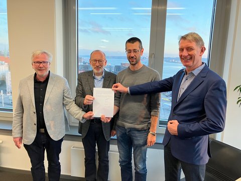 Bernward Völmicke, Stadt Schleswig, Bernd Hannemann, Diakonie Stiftung Schleswig-Holstein, Alexander Opitz, Stadt Schleswig, Kay-Gunnar Rohwer, Diakonie Stiftung Schleswig-Holstein halten einen unterschriebenen Kaufvertrag in der Hand