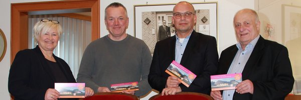 Das Bild zeigt (v.l.n.r.) die Fachbereichsleitung des Fachbereichs Bildung, Kultur und Ordnung Frau Dr. Julia Pfannkuch, Herrn Christian Jensen von der Tischlerei Jensen und die Rechtsanwälte und Notare Karsten und Frank Noetzel. Gemeinsam stehen sie hinter den überreichten Theaterstuhl-Tandems und halten den neuen Spendenflyer "Das Kulturhaus. Die Zukunft. Sind wir." vor.
