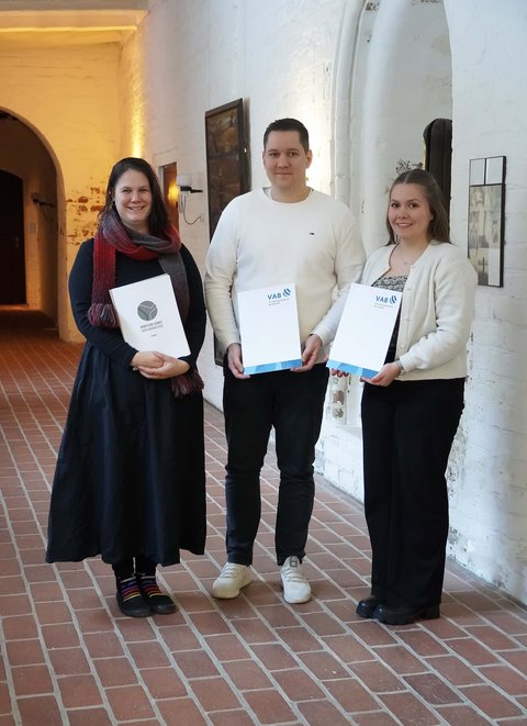 Tahmani Carstensen, Arne Albertsen und Hannah Jürgens mit dem Ausbildungszeugnis im Gang des Grauklosters